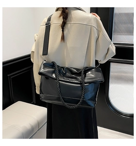 Detail of black large tote bag with woven handles and wide nylon shoulder strap on model