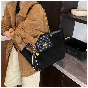 Detail of a black quilted tote bag with gold chain strap and playful charms