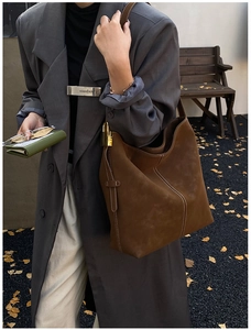 Detail of a brown suede hobo bag with white stitching and a golden padlock accessory