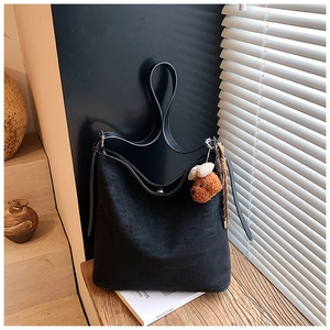 Close-up of black matte bucket bag with a cute brown teddy bear keychain on a wooden desk