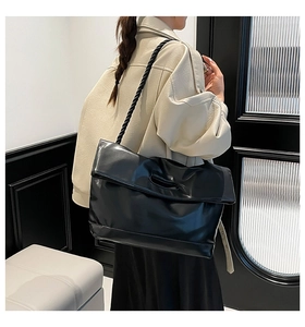 Detail of a large black glossy shoulder bag featuring a unique braided rope strap design
