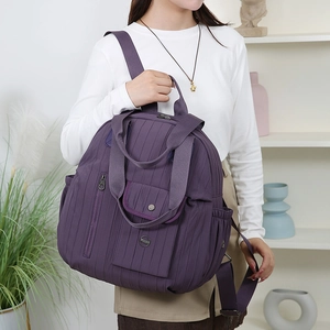 Detail of purple quilted backpack showing vertical stitching texture and front snap pocket