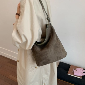 Macro view of olive green frosted suede hobo bag with adjustable strap on trench coat