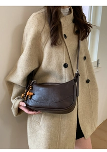 Dettaglio della borsa hobo in pelle testa di moro con pendente in legno su cappotto