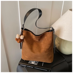 Detail of brown suede tote bag with contrast black straps and a cute plush bear charm