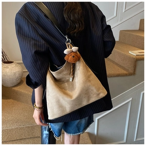 Close-up of khaki suede tote bag featuring a brown plush charm and black leather strap