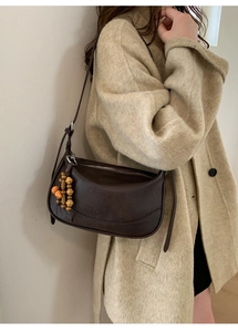 Detail view of a dark brown half-moon underarm bag with wooden bead charm on a beige coat