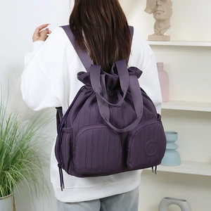 Detail eines lila plissierten Nylon-Rucksacks mit Kordelzug und zwei Reißverschlusstaschen
