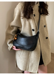 Dettaglio borsa hobo nera minimalista con tracolla regolabile e ciondolo in legno