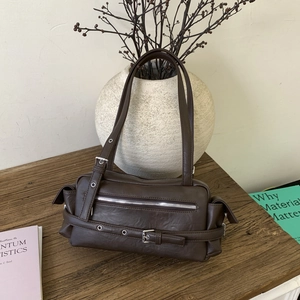 Detail of dark brown leather pillow bag with silver buckles on a wooden table