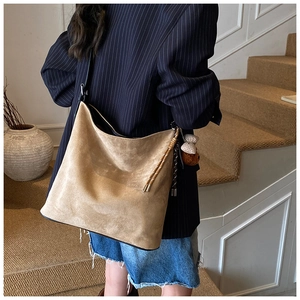 Detail of light brown suede bucket bag featuring woven drawstring and cute bear charm