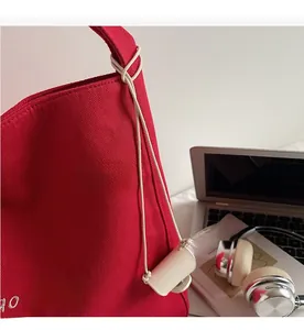 Dettaglio ravvicinato della borsa tote in tela rossa con ricamo bianco e ciondolo