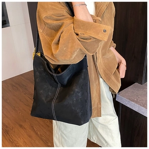 Detail of black suede tote bag with white contrast stitching and gold metal hardware