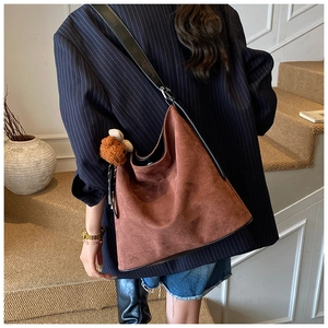Detailed view of a brown suede hobo bag with a cute bear pendant on a striped blazer