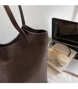 Brown leather tote bag next to a laptop and headphones showing its large capacity and texture