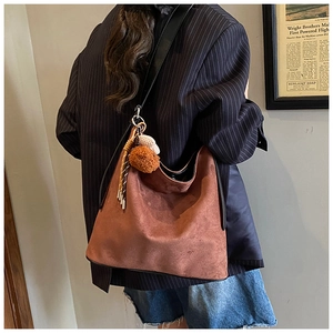 Brown suede hobo bag with wide shoulder strap and plush charms shown on model back