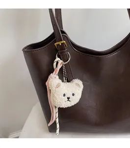 Close-up of cute white teddy bear plush charm with woven lanyard on a brown tote bag