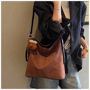 Detail of a brown frosted leather tote bag with a cute plush bear charm on the strap
