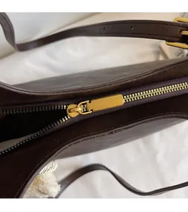 Close-up of smooth gold zipper hardware on deep brown leather tote bag detail