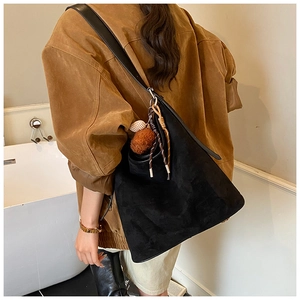 Detail of black suede bucket bag with long leather strap and pompom charm on a model