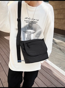 Dettaglio borsa a tracolla in nylon nero con patta e targhetta logo blu in primo piano