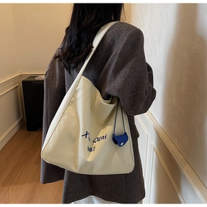 Dettaglio della borsa tote in tela bianco sporco con scritte blu e ciondolo mini pochette
