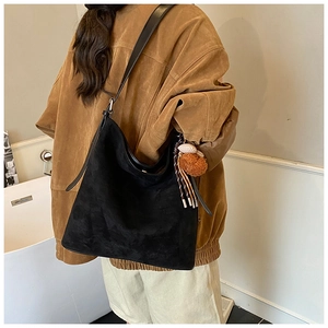 Close-up of black suede tote bag with brown pom-pom charm and adjustable shoulder strap