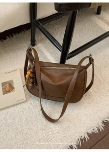 Detail of brown vintage leather shoulder bag with wooden bead charm and silver zipper