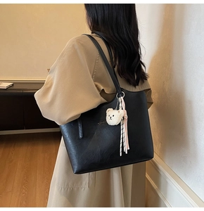 Detail of black leather tote bag featuring a plush bear charm and ribbon accessory