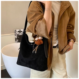 Close-up of a black matte suede hobo bag worn by a model with a brown plush bear charm