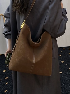 Brown suede hobo bag with contrast stitching and gold buckle shown on model in a long coat
