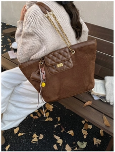 Detail of dark brown suede tote bag with chain strap and charms in an autumn outdoor setting