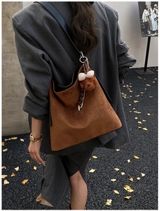 Detail of suede tote bag in dark brown with a cute plush bear charm on gravel ground
