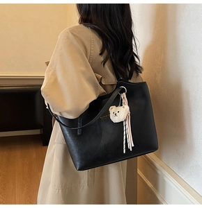 Detailed view of a black large tote bag with a plush bear charm and striped ribbon detail