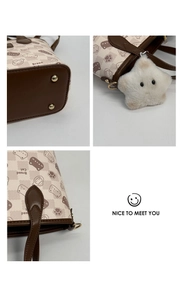 Detail view of cat print tote bag showing metal feet, zipper, and plush star charm