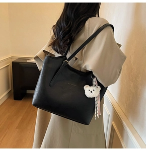 Detail of black leather tote bag featuring a plush bear pendant and striped ribbon accessory