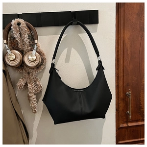 Détail d'un sac hobo noir en forme de croissant suspendu dans un intérieur chaleureux
