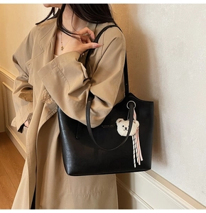 Detail of a large black tote bag with a teddy bear charm on a trench coat model