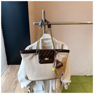 Detail of beige tote bag featuring brown quilted pocket, gold lock, and chain strap