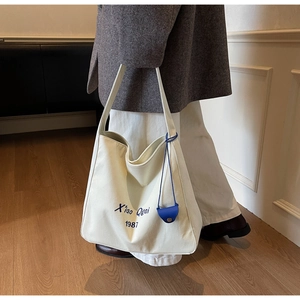 Dettaglio della borsa tote in tela bianco sporco con testo ricamato blu e mini borsellino