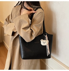 Detail of black leather tote bag with gold logo, plush bear charm and ribbon decoration