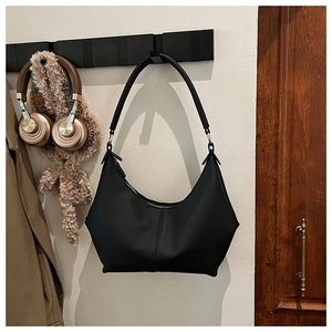 Gros plan du sac hobo noir en croissant avec coutures verticales suspendu au mur