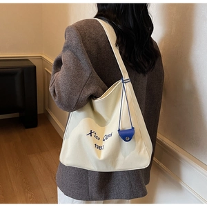 Dettaglio ravvicinato di una borsa tote in tela crema con scritta blu e mini pochette