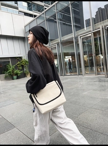 Foto street style di una grande borsa messenger in tela beige con dettagli neri