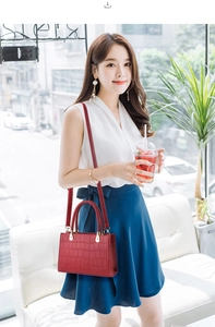 Detail of red crocodile texture handbag held by a model in a bright cafe setting