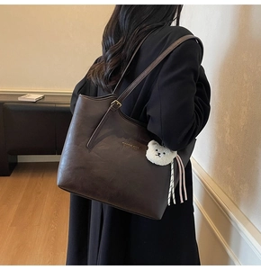 Detail of dark brown tote bag with metal buckle and cute white bear plush charm accessory