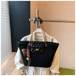 Detail of black tote bag with quilted leather flap, gold lock and chain strap on coat