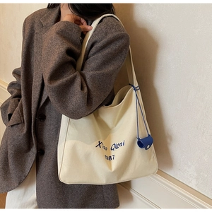 Dettaglio della borsa tote in tela color crema con scritte blu e ciondolo abbinato