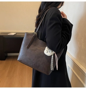 Detail view of large dark brown leather tote bag with gold logo and plush bear charm