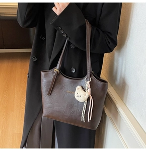 Detail of dark brown leather tote bag with adjustable strap and plush bear pendant accessory